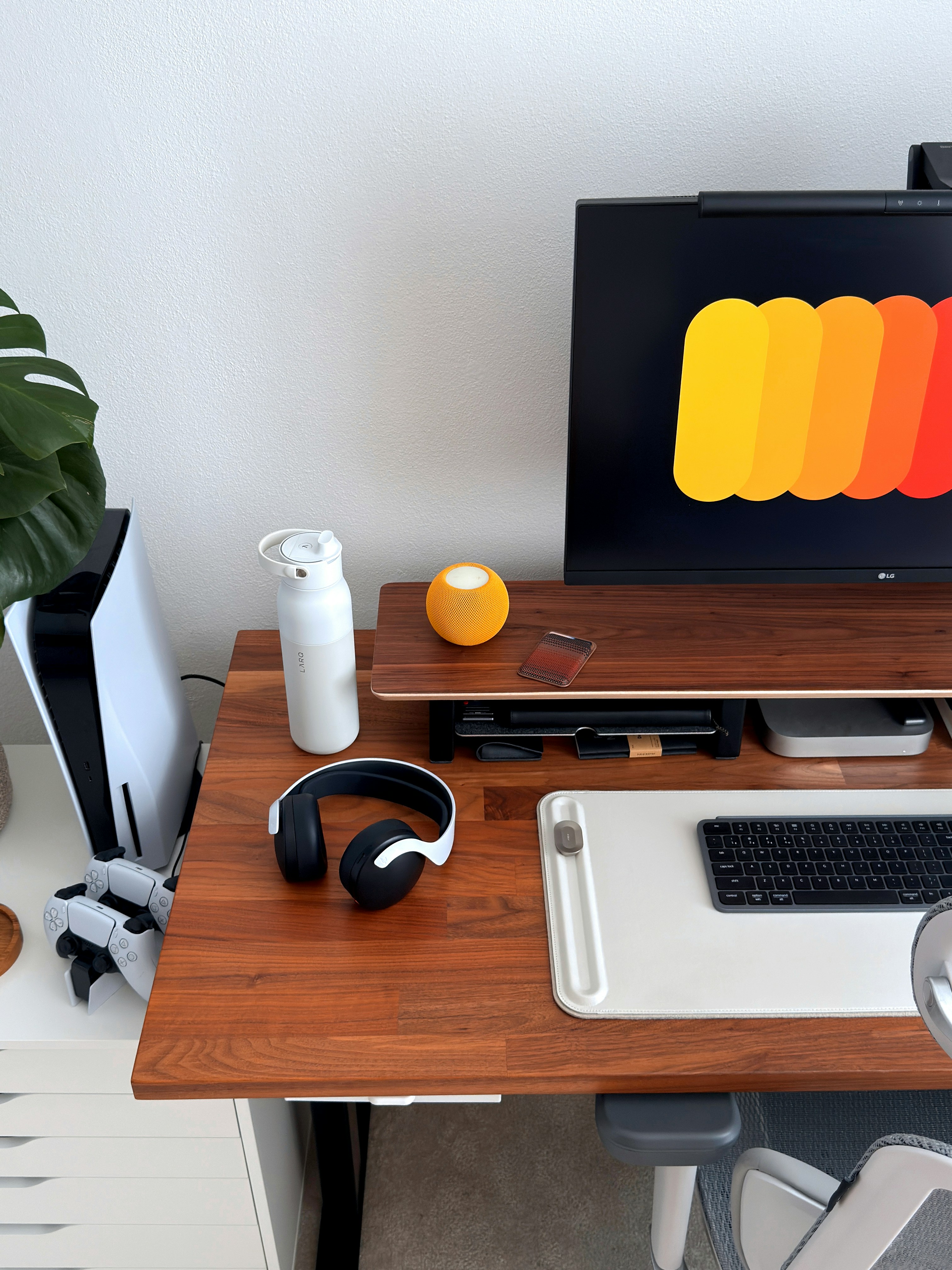 Premium wireless headphones on a dark wooden desk with mechanical keyboard and monitor arm setup